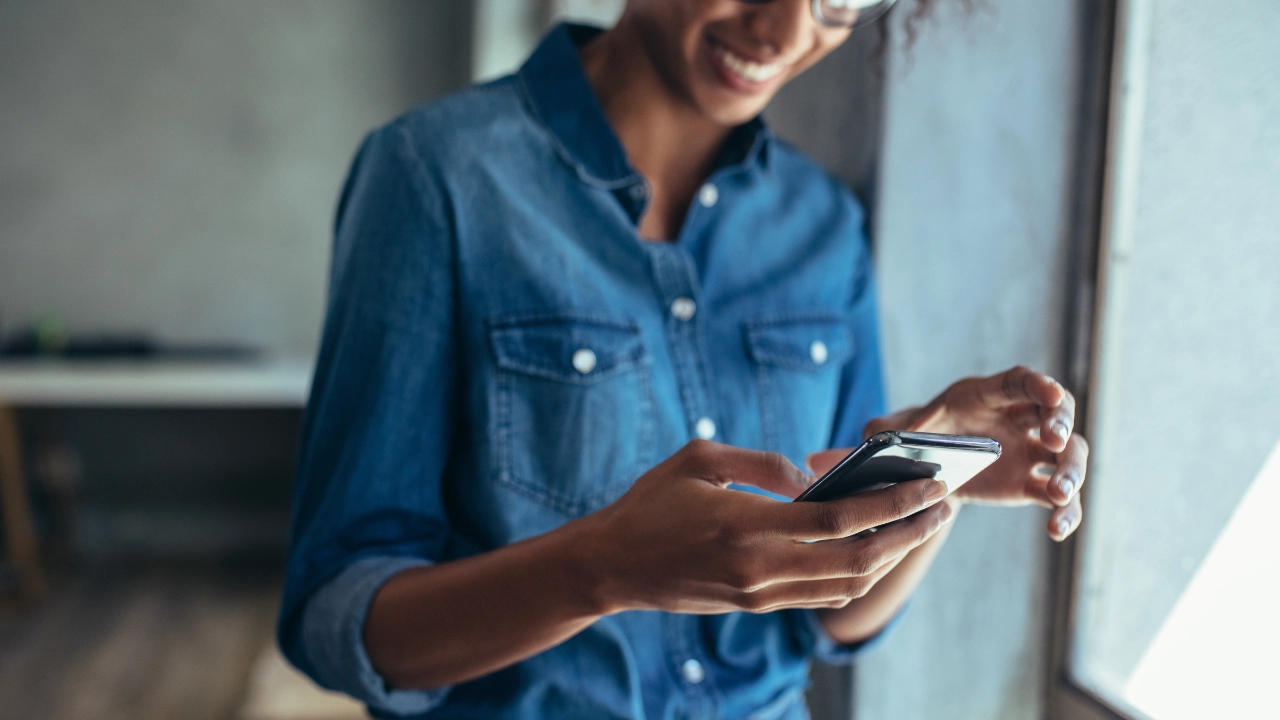 Eine junge Frau schaut lächelnd auf ihr Handy.