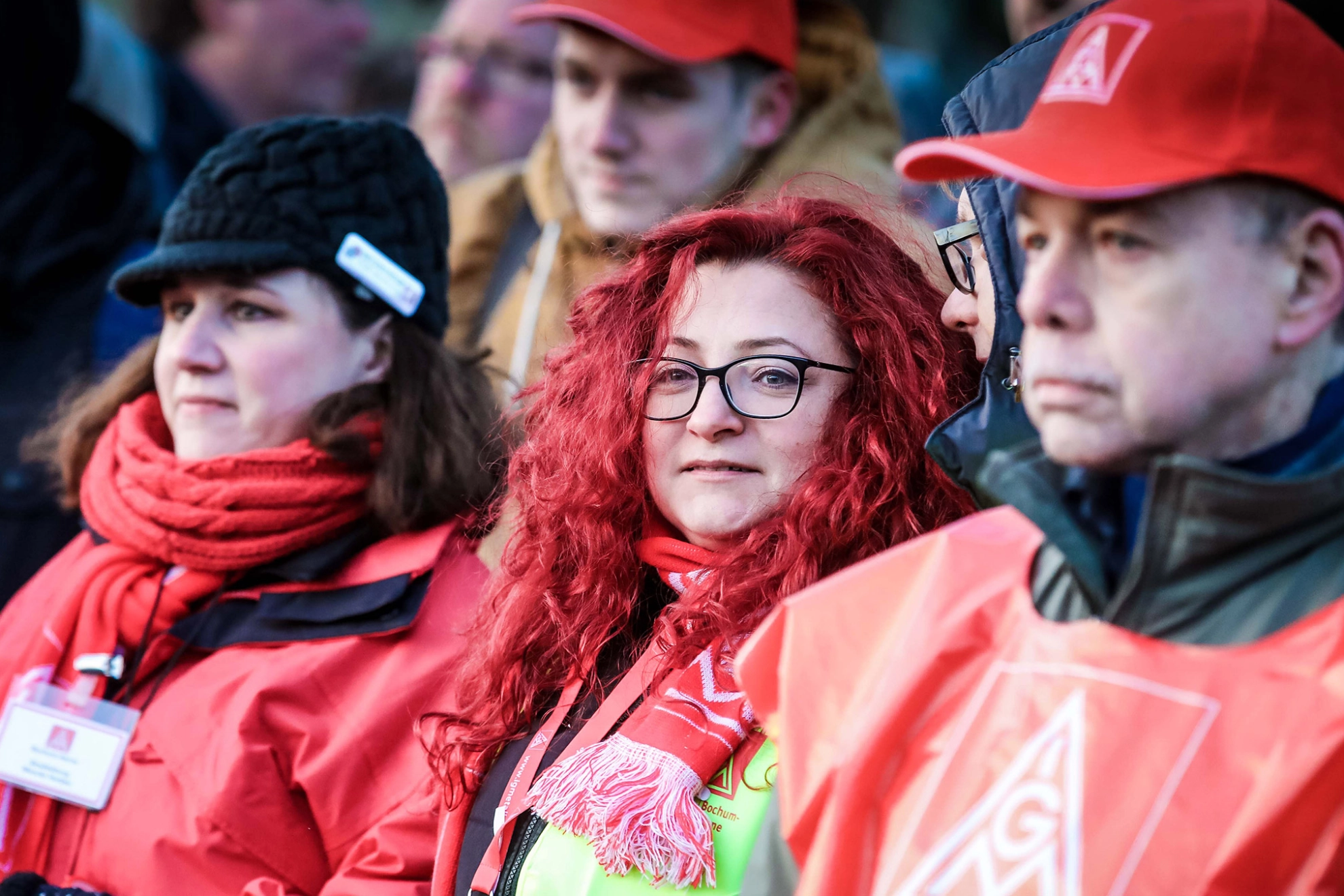 Eine Frau mit roten Locken, dunkler Brille und IG Metall-Schal lächelt in die Kamera.