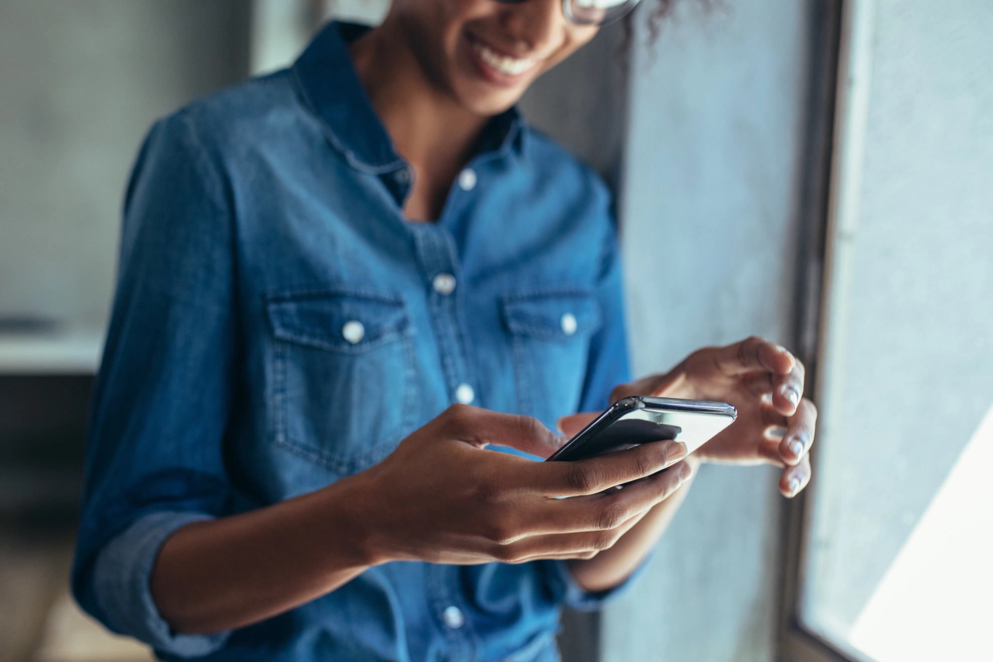 Eine junge Frau schaut lächelnd auf ihr Handy.